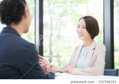 Two businessmen, a man and a woman, having a business meeting at the office; a woman in a suit selling insurance and planning Two businessmen, a man and a woman, having a business meeting at the office; a woman in a suit selling insurance and planning 132598202