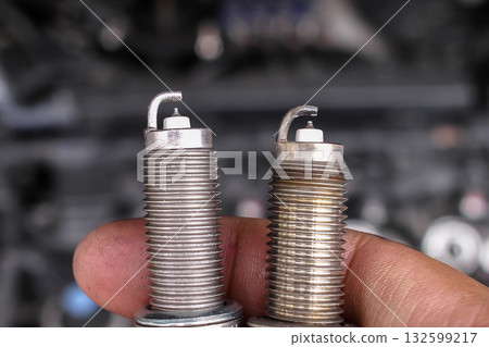 Mechanic hand holding new and used spark plugs side by side 132599217
