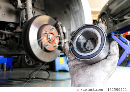Mechanic hand holding new wheel bearing in front of car brake disc 132599221