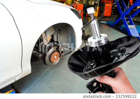 Mechanic hand holding new shock absorber in front of car brake system Mechanic hand holding new shock absorber in front of car brake system 132599222
