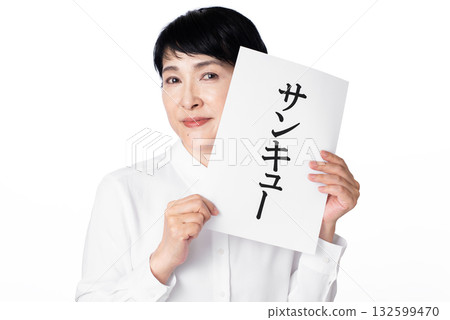 A senior woman wearing a white shirt smiling and holding a piece of paper that says thank you 132599470