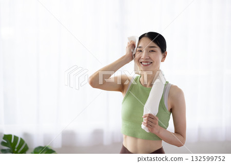 A woman in yoga wear wiping sweat with a towel A woman in yoga wear wiping sweat with a towel 132599752