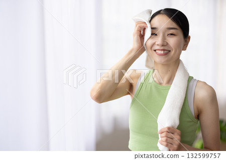 A woman in yoga wear wiping sweat with a towel 132599757