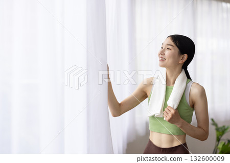 A woman in yoga wear with a towel around her neck smiling by the window A woman in yoga wear with a towel around her neck smiling by the window 132600009