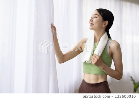 A woman in yoga wear with a towel around her neck smiling by the window A woman in yoga wear with a towel around her neck smiling by the window 132600010