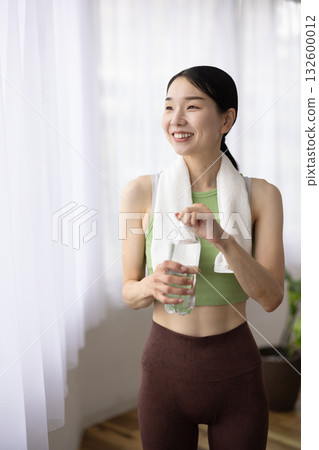 Smiling woman in yoga wear holding a bottle of water Smiling woman in yoga wear holding a bottle of water 132600012