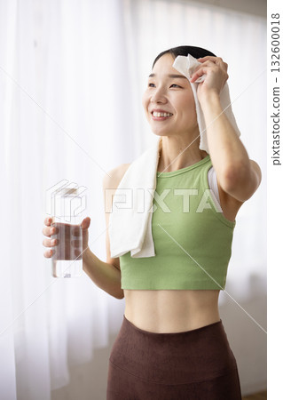 一位身穿瑜珈服的女子手拿一瓶水，正用毛巾擦拭汗水。 132600018