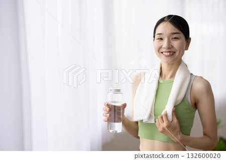 身穿瑜珈服、微笑的女子手裡拿著一瓶水 132600020