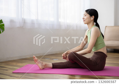 Middle-aged woman wearing wireless earphones stretching on a yoga mat 132600387
