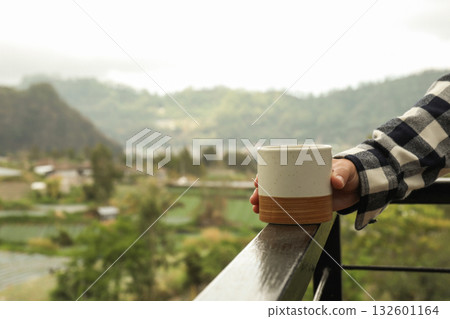 Holding a ceramic cup while admiring the scenic landscape Holding a ceramic cup while admiring the scenic landscape 132601164