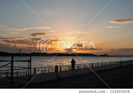 Silhouette of a couple gazing at the sunset over Osaka Bay and the construction site of the Expo site on the opposite shore (date, future, twilight) Silhouette of a couple gazing at the sunset over Osaka Bay and the construction site of the Expo site on the opposite shore (date, future, twilight) 132601658
