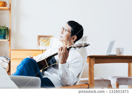 Middle-aged man playing guitar in the living room Middle-aged man playing guitar in the living room 132601871