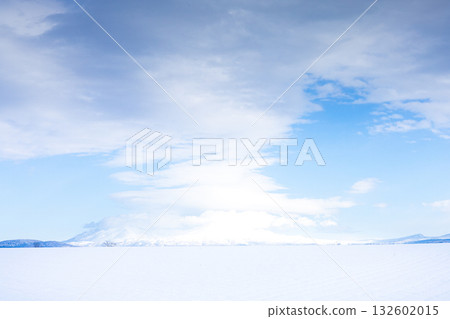 A simple landscape of mysterious clouds, blue sky, snowy fields and snow-capped mountains 132602015