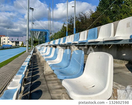 Empty blue and white stadium seats line a vibrant blue running track, evoking anticipation for sports events and gatherings Empty blue and white stadium seats line a vibrant blue running track, evoking anticipation for sports events and gatherings 132602598