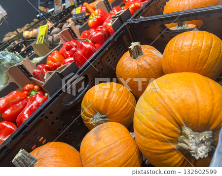 Fresh vibrant orange pumpkins and crisp red bell peppers displayed in market crates at a busy grocer's, emphasizing healthy seasonal produce and autumn harvest Fresh vibrant orange pumpkins and crisp red bell peppers displayed in market crates at a busy grocer's, emphasizing healthy seasonal produce and autumn harvest 132602599