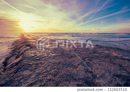 Seascape in the evening. Sunset over the Atlantic Ocean. A stone breakwater in the ocean. Coast at Costa da Caparica, Almada, Portugal Seascape in the evening. Sunset over the Atlantic Ocean. A stone breakwater in the ocean. Coast at Costa da Caparica, Almada, Portugal 132603510