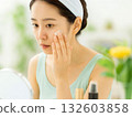 A woman doing skin care in front of a mirror in a bright room 132603858