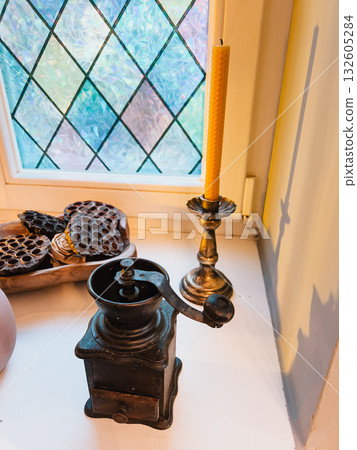 Old coffee grinder resting on windowsill beside beeswax candle and dried lotus pods in wooden bowl, bathed in soft sunlight from stained glass window. Vintage coffee grinder near beeswax candle Old coffee grinder resting on windowsill beside beeswax candle and dried lotus pods in wooden bowl, bathed in soft sunlight from stained glass window. Vintage coffee grinder near beeswax candle 132605284