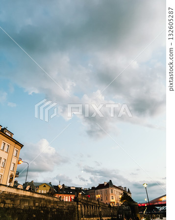 Scenic Krakow cityscape featuring the Vistula River embankment and historic buildings illuminated by stunning sunset under dramatic sky. Krakow cityscape highlighting Vistula River embankment Scenic Krakow cityscape featuring the Vistula River embankment and historic buildings illuminated by stunning sunset under dramatic sky. Krakow cityscape highlighting Vistula River embankment 132605287