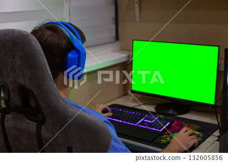Green screen monitor for computer industry project. Technology and advertising concept featuring a green screen in front of a gamer wearing headphones while sitting at computer Green screen monitor for computer industry project. Technology and advertising concept featuring a green screen in front of a gamer wearing headphones while sitting at computer 132605856