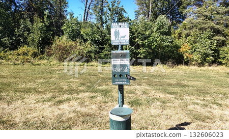 dog waste collection station with plastic bags and a trash can in a public park or along a walking trail for pets and dog owners, caring for the local ecology and hygiene of a dog-friendly environment dog waste collection station with plastic bags and a trash can in a public park or along a walking trail for pets and dog owners, caring for the local ecology and hygiene of a dog-friendly environment 132606023