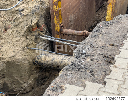 Open construction trench exposing utility pipes and electrical cables, secured by metal shoring for urban infrastructure repair and maintenance Open construction trench exposing utility pipes and electrical cables, secured by metal shoring for urban infrastructure repair and maintenance 132606277