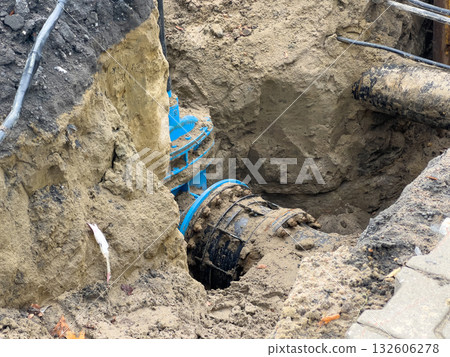 Deep excavated trench revealing large blue and black utility pipes and cables during essential urban infrastructure maintenance and underground repair work Deep excavated trench revealing large blue and black utility pipes and cables during essential urban infrastructure maintenance and underground repair work 132606278