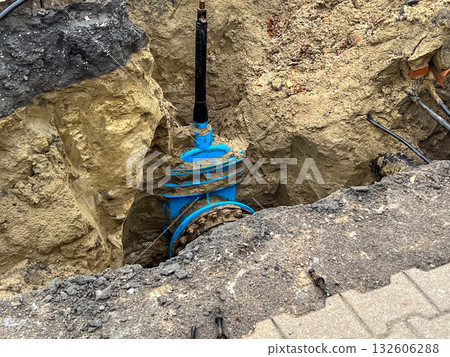 Essential blue water main pipe and valve exposed in deep trench for critical urban utility infrastructure repair and maintenance project Essential blue water main pipe and valve exposed in deep trench for critical urban utility infrastructure repair and maintenance project 132606288