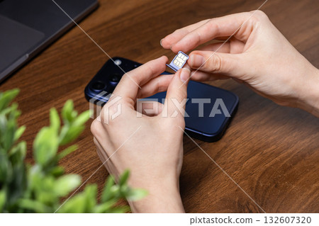 Hands holding a SIM card and tray, preparing for insertion into a smartphone, symbolizing mobile connectivity and digital telecommunication Hands holding a SIM card and tray, preparing for insertion into a smartphone, symbolizing mobile connectivity and digital telecommunication 132607320