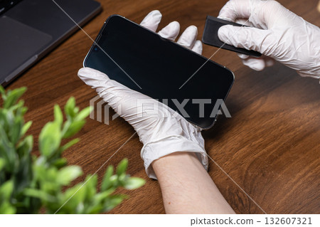 Hands wearing white gloves carefully applying a new screen protector to a modern smartphone, demonstrating essential device protection and meticulous digital gadget care Hands wearing white gloves carefully applying a new screen protector to a modern smartphone, demonstrating essential device protection and meticulous digital gadget care 132607321