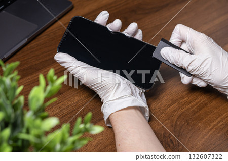 Gloved hands carefully applying a protective screen film to a modern smartphone, symbolizing device care and technology maintenance for everyday use 132607322