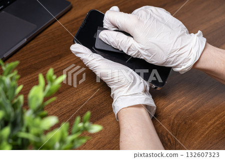 Hands in white gloves carefully cleaning a smartphone screen with a cloth, demonstrating crucial digital device hygiene and germ prevention Hands in white gloves carefully cleaning a smartphone screen with a cloth, demonstrating crucial digital device hygiene and germ prevention 132607323