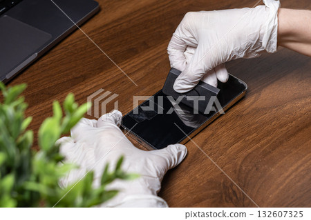 Person in white gloves carefully applies a transparent screen protector film onto a modern smartphone, ensuring optimal display protection and device longevity Person in white gloves carefully applies a transparent screen protector film onto a modern smartphone, ensuring optimal display protection and device longevity 132607325