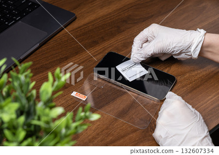 Hand in white glove uses a Dust Remover sticker on a smartphone display, preparing for screen protector installation to ensure device safety Hand in white glove uses a Dust Remover sticker on a smartphone display, preparing for screen protector installation to ensure device safety 132607334