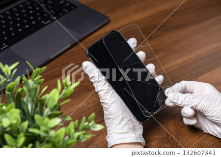 Gloved hands carefully remove a shattered tempered glass screen protector from a modern smartphone, highlighting essential device repair and protection 132607341