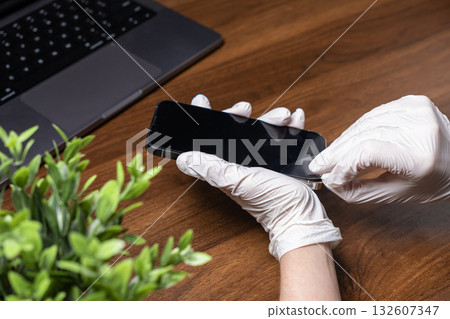 Hands in white gloves applying a screen protector to a modern smartphone, ensuring device longevity, digital hygiene, and enhanced electronic protection Hands in white gloves applying a screen protector to a modern smartphone, ensuring device longevity, digital hygiene, and enhanced electronic protection 132607347