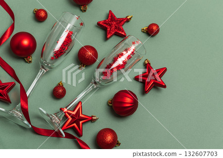 Champagne Flutes with Red Christmas Ornaments and Ribbon on Green Background Champagne Flutes with Red Christmas Ornaments and Ribbon on Green Background 132607703