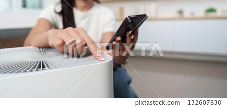 Technology and Home Automation. Young woman controlling air purifier with smartphone. Technology and Home Automation. Young woman controlling air purifier with smartphone. 132607830