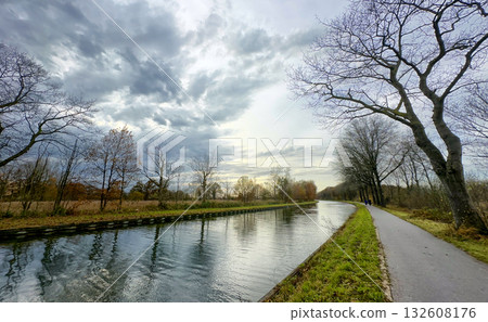 A Serene and Calm Canal Scene with an Overcast Sky and Barren Trees in the Background 132608176