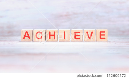 The word achieve is spelled out using red letters on wooden toy blocks. It suggests achievement, setting goals, and working towards success 132609372