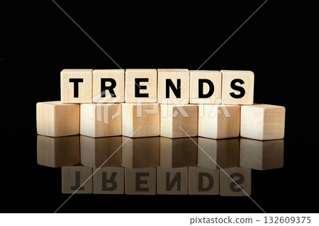 Seven wooden letter blocks stacked on a shiny, reflective surface spell out the word TRENDS against a plain black background. The reflection mirrors the word below 132609375