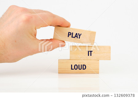 A person uses their hand to place a block labeled PLAY atop two others that say IT and LOUD, building up the message in a close up, minimalistic style A person uses their hand to place a block labeled PLAY atop two others that say IT and LOUD, building up the message in a close up, minimalistic style 132609378