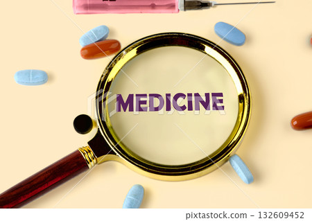 Magnifying glass enlarges the word MEDICINE surrounded by colorful pills and a syringe. The arrangement on the cream background hints at medical research and health Magnifying glass enlarges the word MEDICINE surrounded by colorful pills and a syringe. The arrangement on the cream background hints at medical research and health 132609452