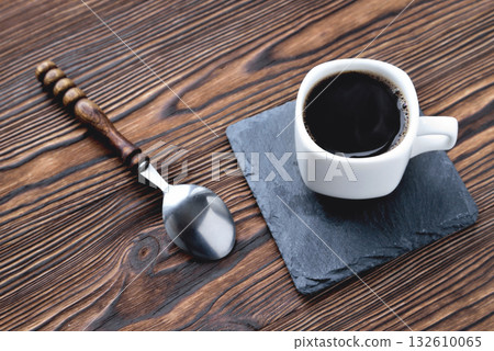 white cup with coffee on a stone stand, vintage coffee spoon, wooden natural background close up copy 132610065