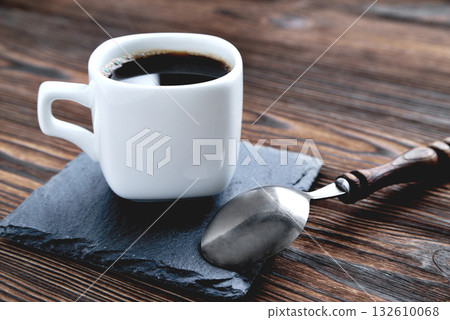 white cup with coffee on a stone stand, vintage coffee spoon, wooden natural background close up copy space 132610068
