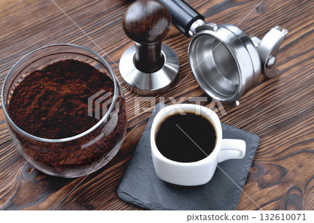 coffee in a cup on a stone stand, a glass jar with coffee and coffee accessories tempera and a coffee machine horn, wooden natural background 132610071
