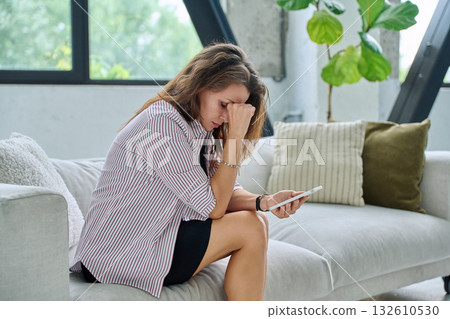 Sad serious middle aged woman with smartphone sitting on sofa 132610530