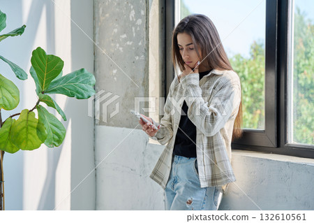 Serious teenage female standing at home reading texting on smartphone 132610561