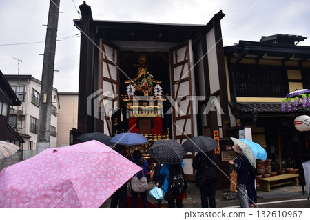 日本岐阜縣高山市:春季高山祭期間,華麗的美食攤位因雨水而隱藏在倉庫中。遊客在傘下享受祭典。 日本岐阜縣高山市:春季高山祭期間,華麗的美食攤位因雨水而隱藏在倉庫中。遊客在傘下享受祭典。 132610967