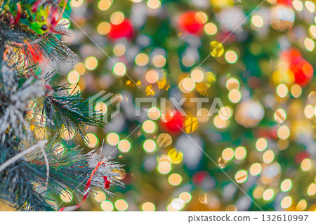 A blurry, out-of-focus photograph of a decorated Christmas or New Year's tree, adorned with ornaments and garlands that glow and sparkle, creating a bokeh effect. Background shot, out of focus 132610997
